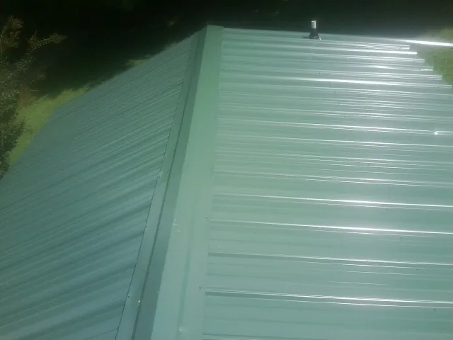 New green metal panels meeting at the ridge of a roof — Flat Roof Repair work by our crew in Great Falls